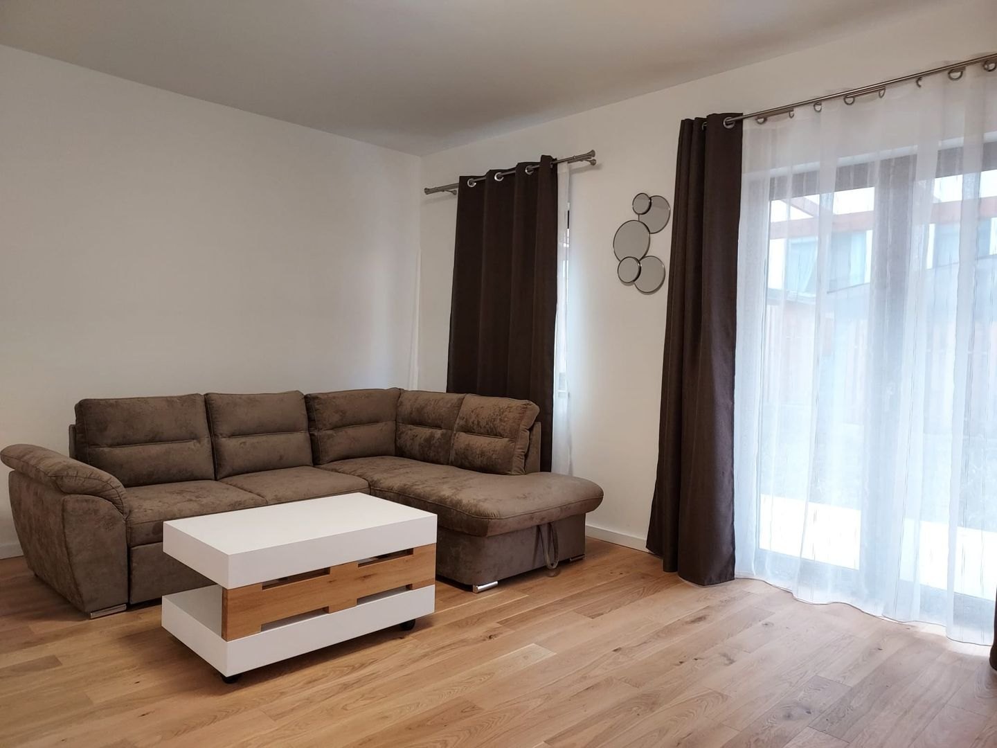 Livingul duplexului, cu canapea de colț, parchet de stejar și ferestrele largi spre curte