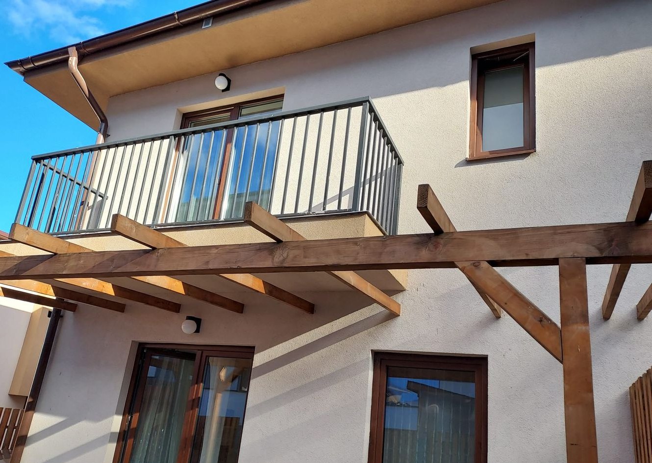 Terasa acoperită de pergola de lemn și balconul de la etaj